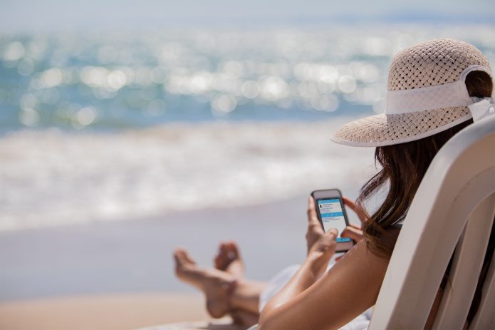 Девушка сидит на берегу моря с мобильным телефоном